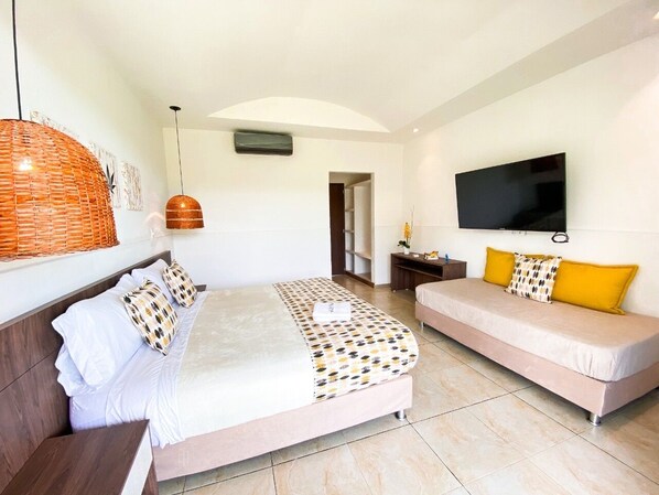 A bedroom with a bed, a sofa, a TV, and a wall-mounted air conditioner.