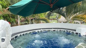 A hot tub surrounded by stone tiles and a green umbrella. - Hotel Zensi 420 (Lejanías)