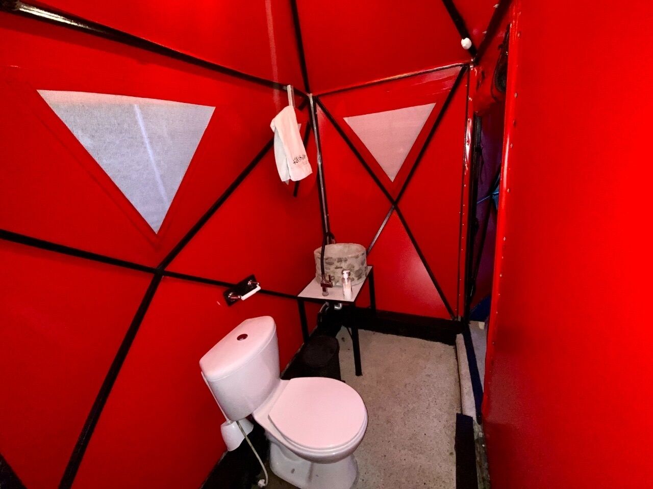 A small, red-walled bathroom with a white toilet, a towel hanging on the wall, and a small table with a trash bin.