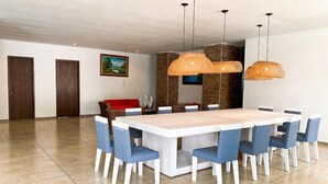 A spacious dining area with a large rectangular table surrounded by blue upholstered chairs, a rustic woven light fixture above, and a stone accent wall. - Hotel Zensi 420 (Lejanías)