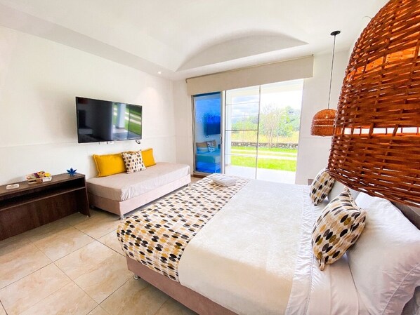 Un dormitorio con cama, televisor, sofá, ventana y una silla de mimbre.