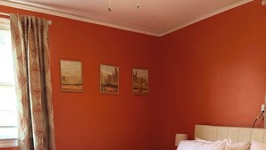 Une chambre avec un grand lit, un plancher en bois et trois tableaux accrochés au mur.