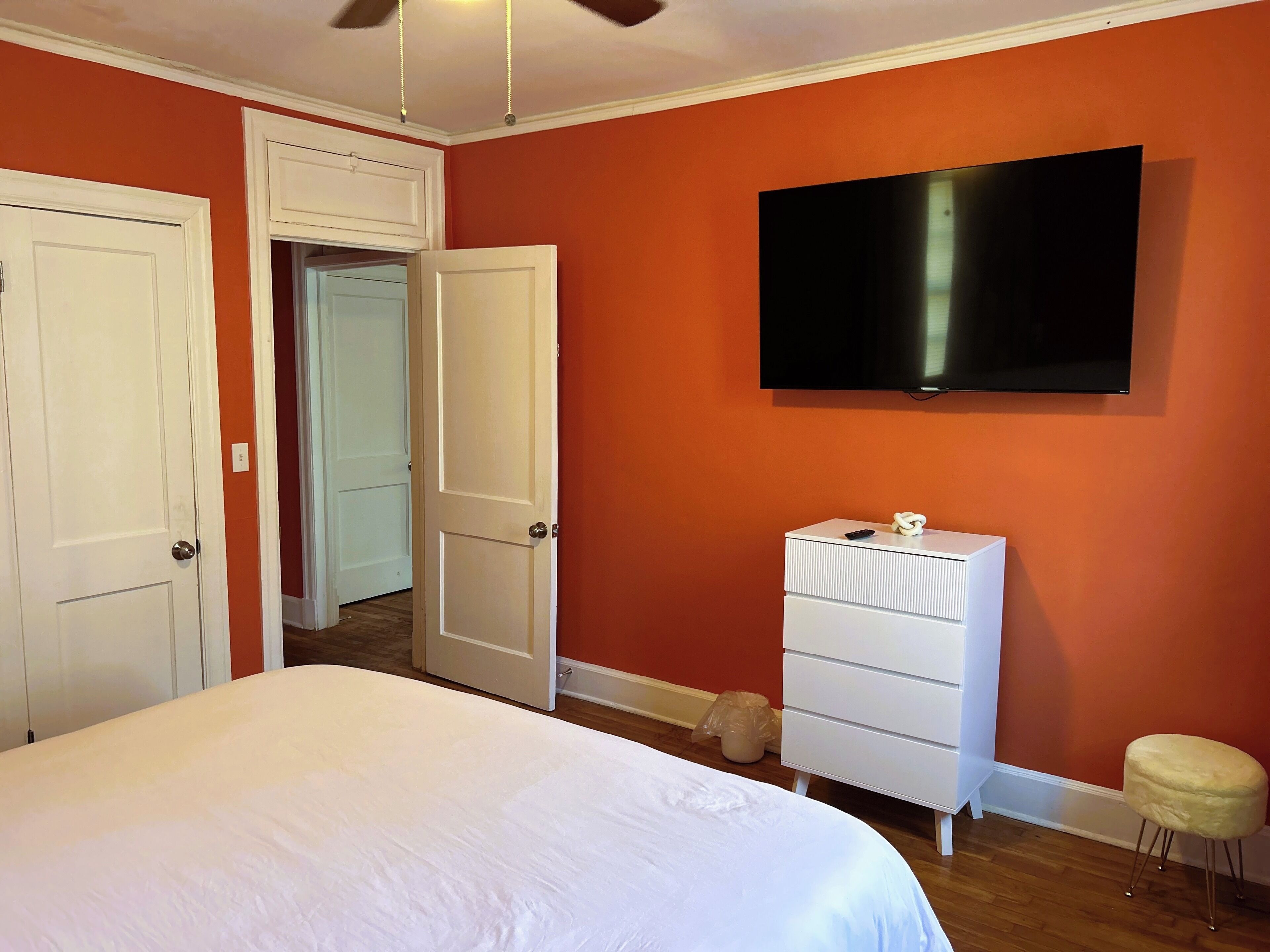 A bedroom with a bed, a dresser, a television, and a door leading to another room.