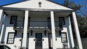 Un bâtiment à deux étages doté d’une façade symétrique, d’une entrée centrale avec une porte noire et d’un balcon au deuxième étage.