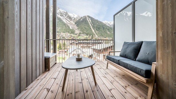 A wooden deck with a round table and a sofa, overlooking a mountainous landscape. - Kotibe- Lovely apartment in Chamonix (Chamonix-Mont-Blanc)