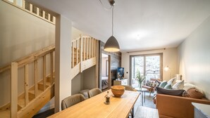 A modern interior with a wooden staircase, a dining area with a wooden table, and a cozy seating area with a sofa and cushions. - Kotibe- Lovely apartment in Chamonix (Chamonix-Mont-Blanc)