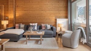 Een moderne woonkamer met een houten wand, een grijze bank en een glazen deur die leidt naar een balkon.
