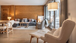 Een moderne woonkamer met een houten wand, een zithoek, een salontafel en een groot raam met gordijnen.
