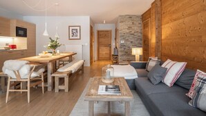 Een gezellige woonkamer met een houten bank, een eettafel met bankjes en een keuken met houten kastjes en een magnetron.