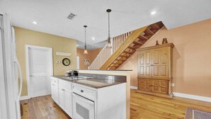 A kitchen with a wooden staircase, white cabinetry, and a clock on the wall.