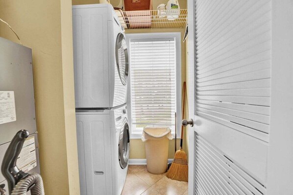 A laundry area with a washing machine, a trash bin, and a broom. - Top-Floor Gulf Views, Pool & Pet-Friendly | Off the Clock (Port St. Joe)