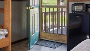 A room with a wooden door leading to a balcony, a small kitchenette with a refrigerator, and a wooden shelf with towels. - Cozy Cabin1 Within Campground (Mifflinburg)