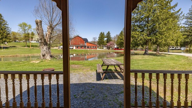 A gazebo with a view of a lake, picnic table, and a red building in the background. - Cozy Cabin1 Within Campground (Mifflinburg)