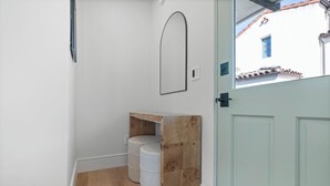 A hallway with a wooden bench, a white door, and a window with a view of a building with a blue window.