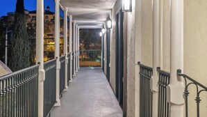A covered outdoor corridor with a railing, columns, and lights.