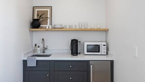 A compact kitchen with a microwave, coffee maker, and a shelf with glassware.