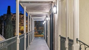 A covered corridor with a railing, columns, and lights.