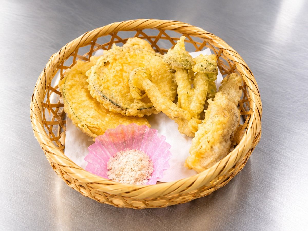 A basket containing fried food items and a pink paper cup with a granular substance, placed on a metallic surface.