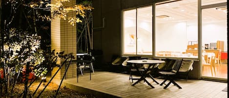An outdoor patio with tables and chairs, a brick wall, and a building with large windows in the background.