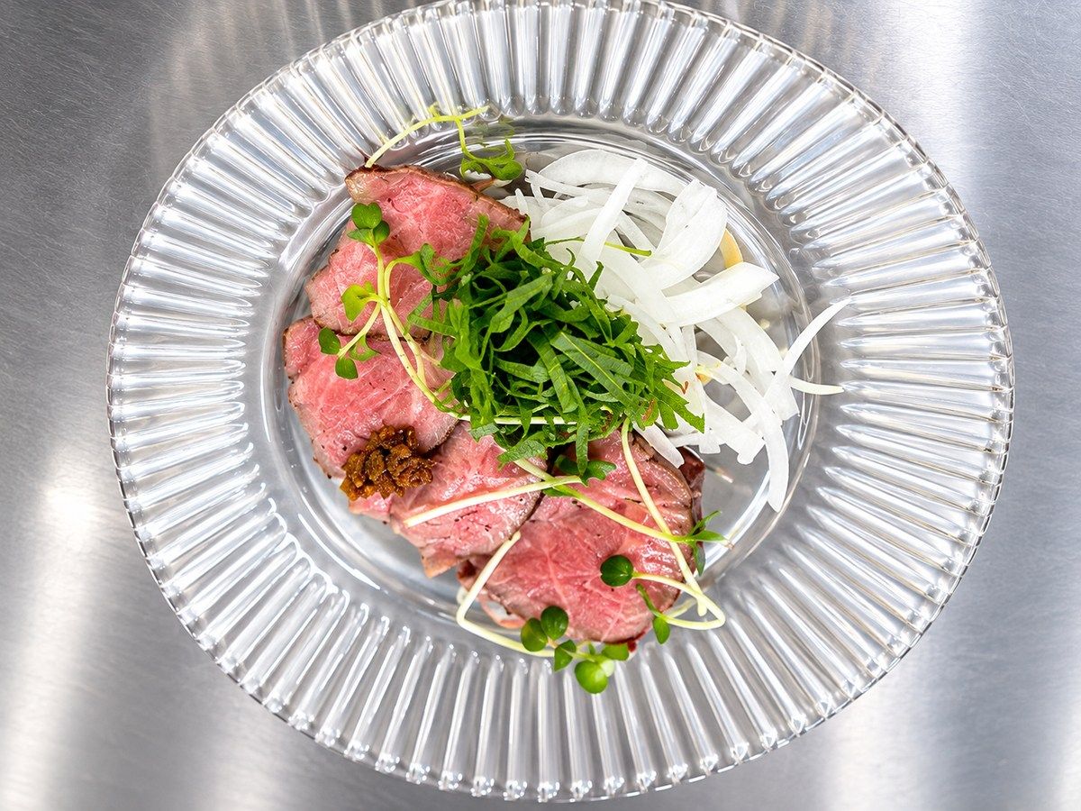 Eine transparente Glasscheibe mit geschnittenem Fleisch, gehobelten weißen Gemüsesorten und grüner Dekoration.