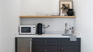 Een keuken met een magnetron, koffiezetapparaat en een plank met glazen en een plant.