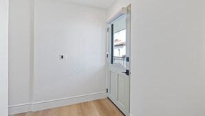 Een gang met witte muren en houten vloeren, leidend naar een deur met uitzicht op een balkon.