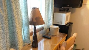 A wooden dining table with a remote control, a white cup, and a lamp. A television is mounted on the wall above the table. - Holiday Motel (Manistique)