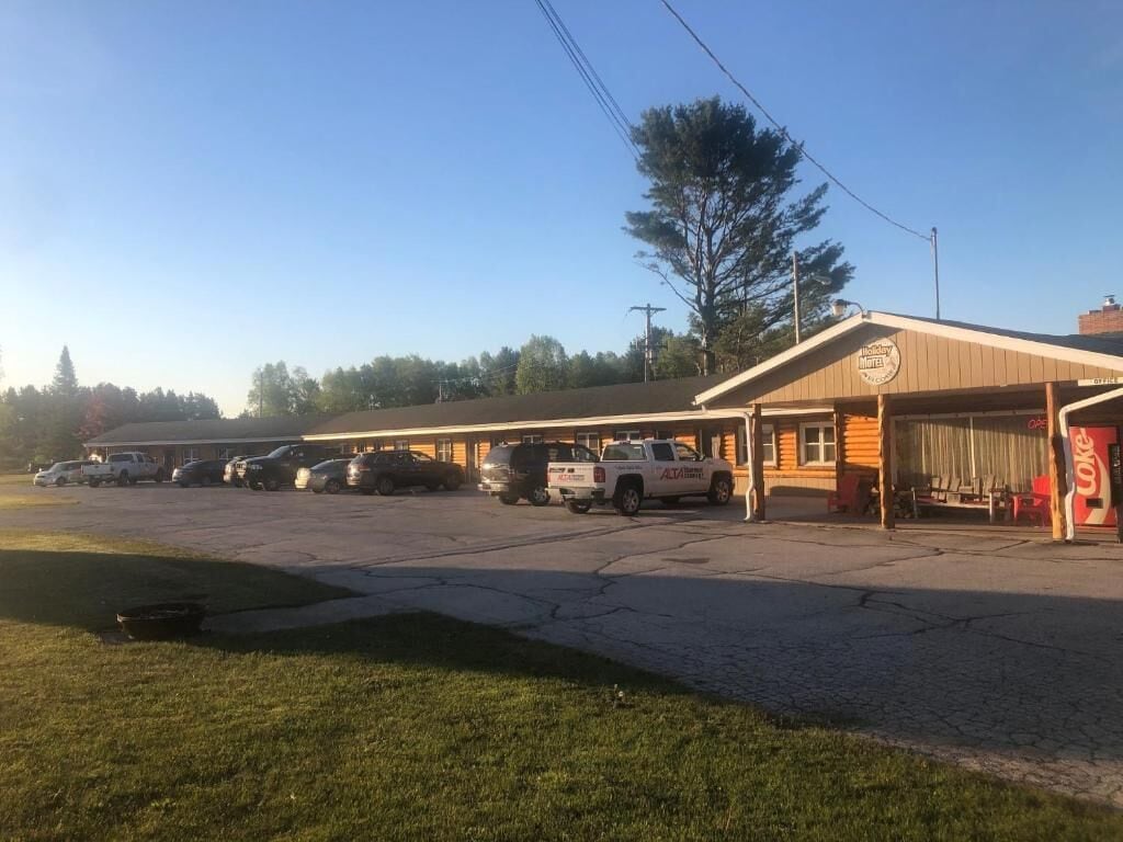 Un motel con una fila de vehículos estacionados, una zona de estacionamiento cubierta y un letrero de Coca-Cola.
