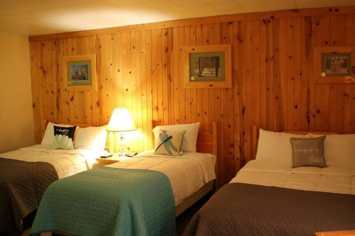 A room with two beds, wooden paneling on the walls, framed pictures, and a lamp on the nightstand.