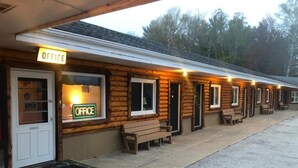 A row of log cabins with 'OFFICE' signs, wooden benches, and a concrete pathway. - Holiday Motel (Manistique)