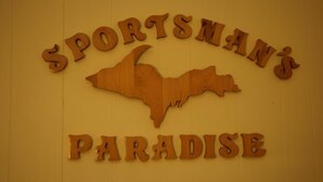 A wooden sign with the text "SPORTSMAN'S PARADISE" and a bat silhouette. - Holiday Motel (Manistique)
