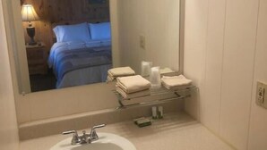 A bathroom with a white sink, mirror, and vanity. There are towels and toiletries on the vanity. - Holiday Motel (Manistique)