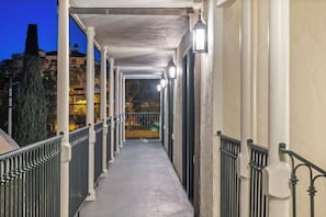 Un corredor cubierto con barandilla, columnas e iluminación en la pared.
