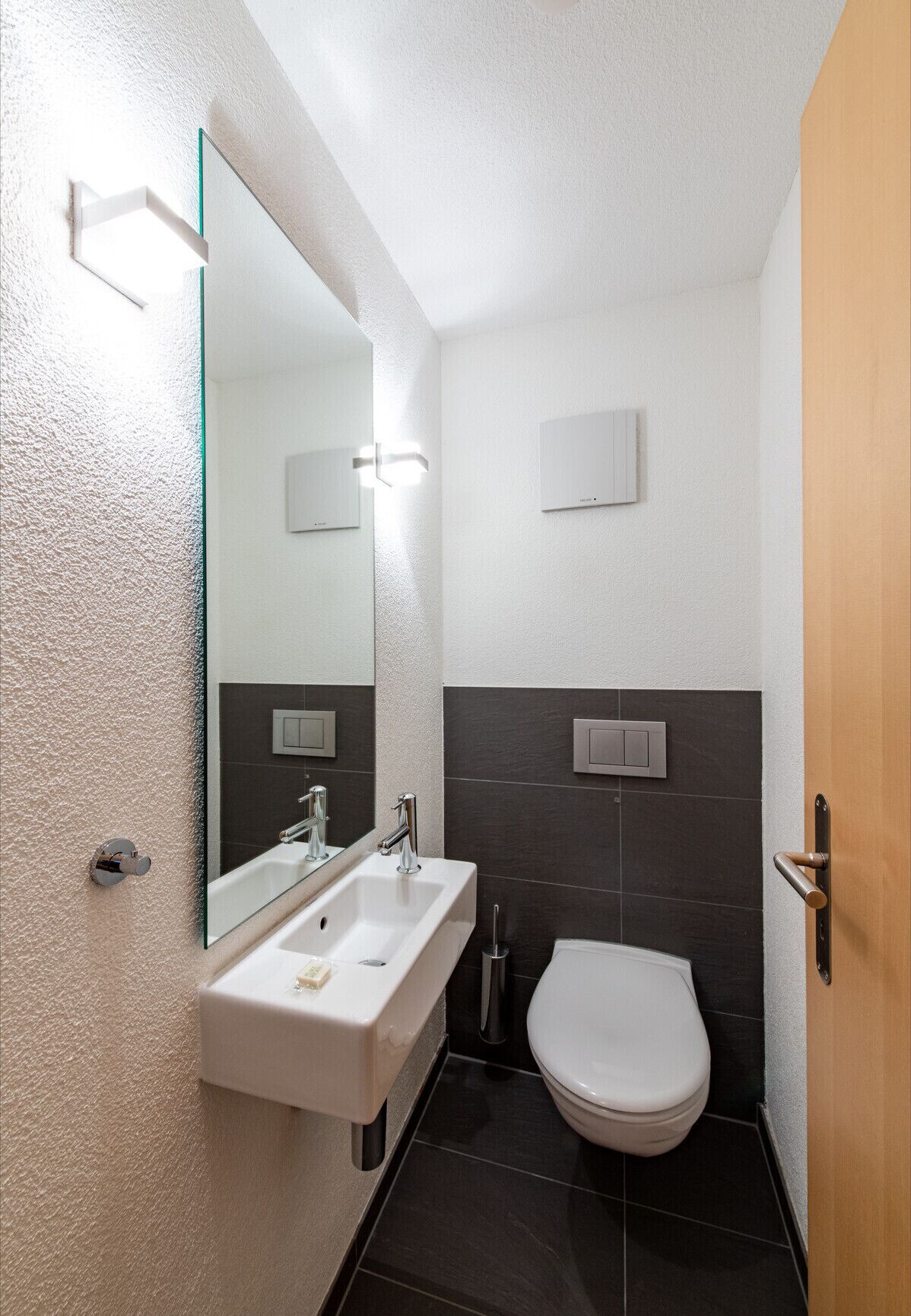 Een kleine badkamer met een wit wastafel, een spiegel, een toilet en een deur.