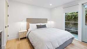 Un dormitorio moderno con una cama grande, lámparas de noche y vistas a zonas verdes a través de una puerta corredera.