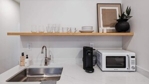 Una cocina moderna con un lavamanos de acero inoxidable, un microondas blanco y una cafetera.