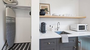Moderni keittiö, jossa on valkoinen työtaso, kahvinkeitin, mikroaaltouuni ja pesuallas.