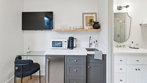 A compact kitchenette with a microwave, coffee maker, and glassware on a white countertop.