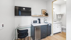A compact kitchen with a microwave, coffee maker, and a glass table with a chair.