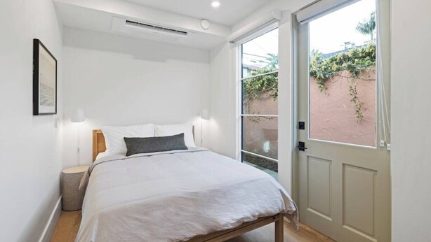 A bedroom with a bed, bedside lamps, a small bedside table, and a door leading to an outdoor area.