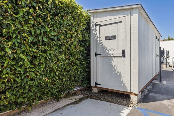 A white utility shed with a door and a sign that reads "AIR MACHINE" next to a well-maintained hedge. - Casa Jardin - Studio 3 (Santa Barbara)