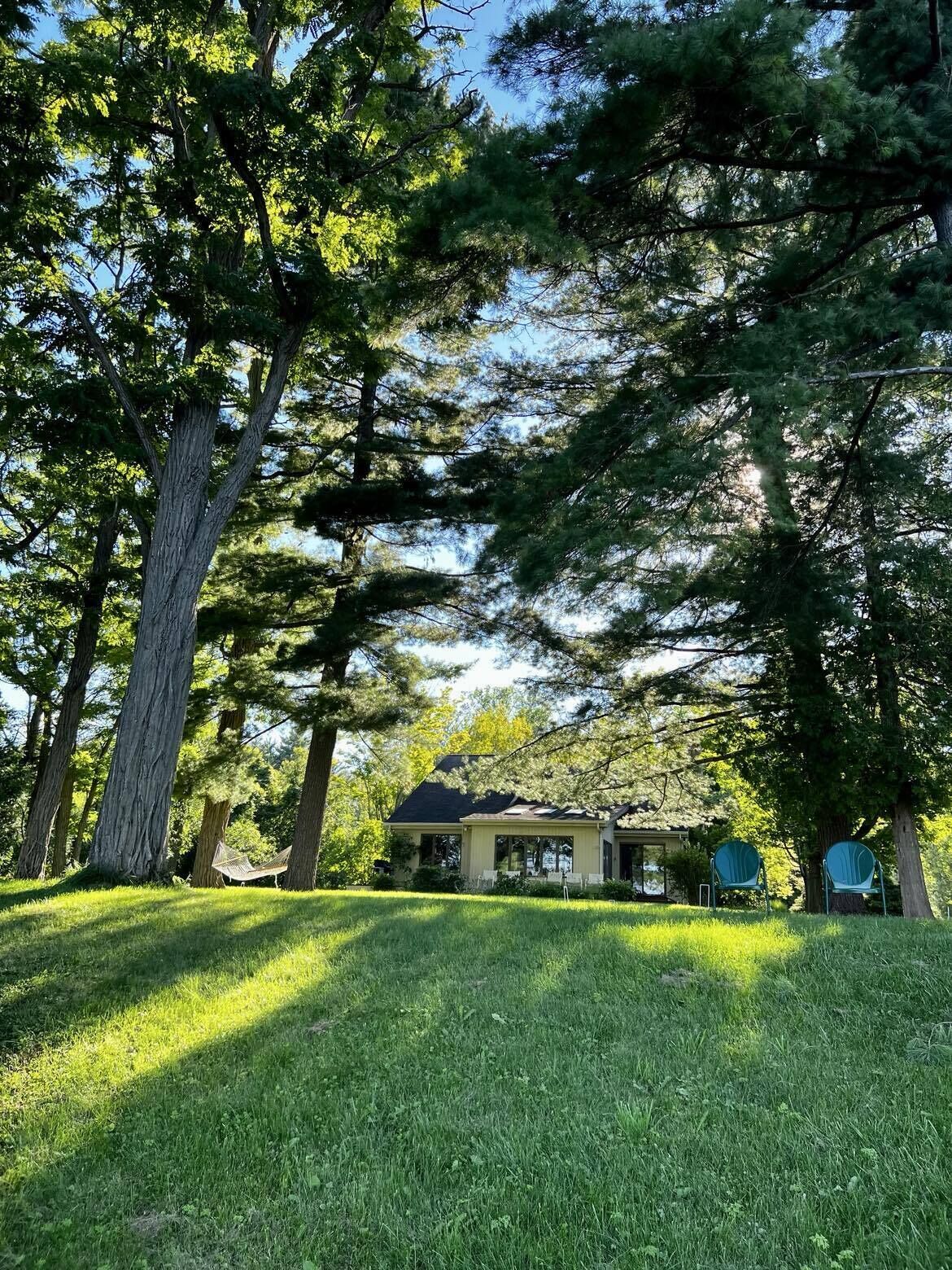 Une maison entourée de grands arbres, avec une pelouse bien entretenue et deux chaises au premier plan.