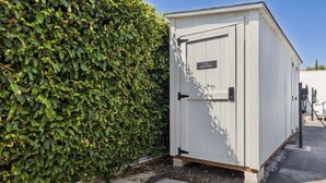 Un cobertizo blanco con una puerta que dice 'AIR MACHINE' junto a un seto verde frondoso.