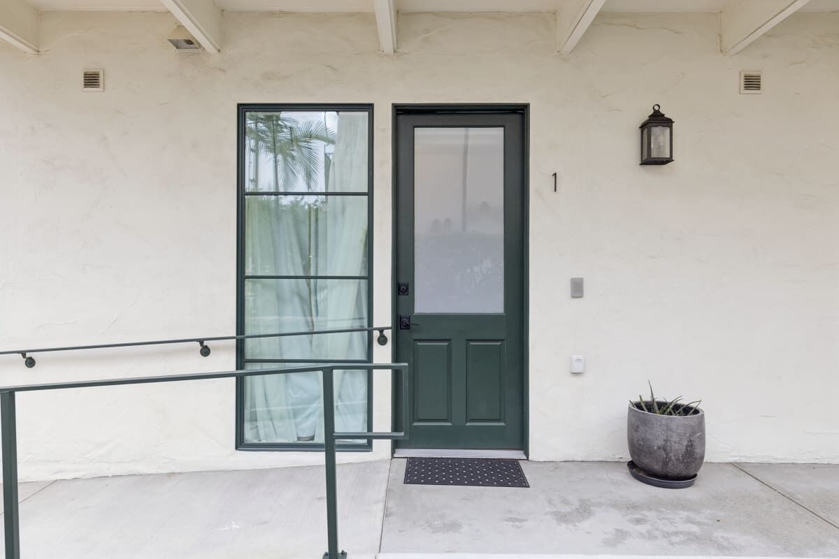 A building entrance with a green door, a potted plant, and a metal railing.
