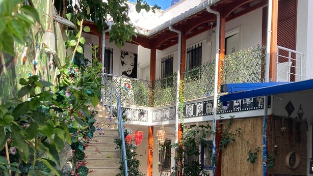 Un patio con una escalera que lleva a un balcón, rodeado de plantas en macetas y mobiliario de exterior.