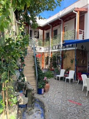A courtyard with a staircase leading to a balcony, surrounded by potted plants and outdoor seating.
