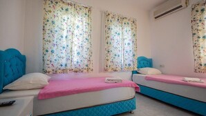 Una habitación con dos camas, cada una con cabecero azul y colcha rosa. Se observa un equipo de aire acondicionado en la pared.