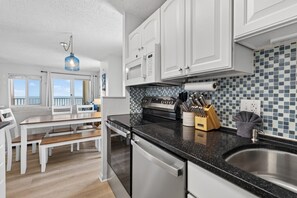 A modern kitchen with white cabinets, a black countertop, and a view of the ocean. - Huge Corner Balcony |Sunrise Ocean Views|Pool 407 (Virginia Beach)