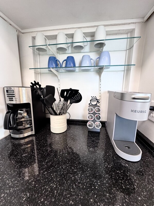 A kitchen with a coffee maker, utensils, and a mug rack.