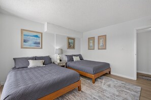 Quarto com duas camas, uma mesa de cabeceira com abajur e quadros nas paredes.